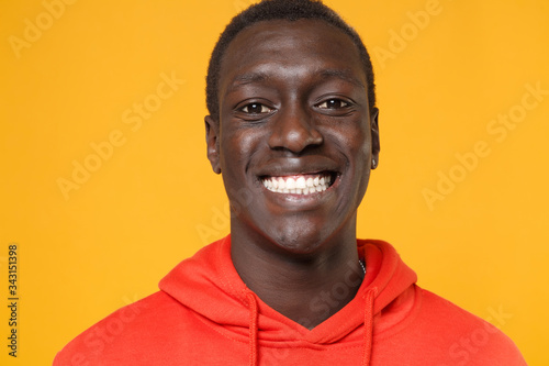 Close up of smiling young african american man guy in red streetwear hoodie posing isolated on yellow background studio portrait. People emotions lifestyle concept. Mock up copy space. Looking camera. © ViDi Studio
