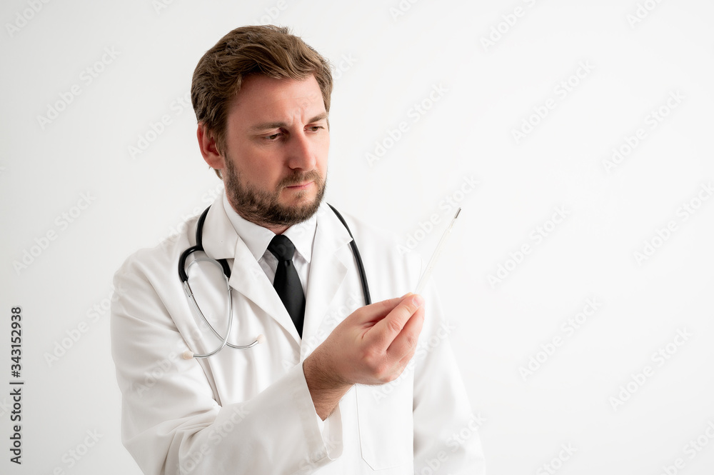 Male doctor with stethoscope in medical uniform is looking at the thermometer Male doctor with stethoscope in medical uniform is looking at the thermometer