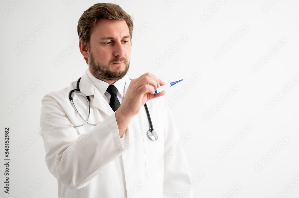 Male doctor with stethoscope in medical uniform is looking at the digital thermometer Male doctor with stethoscope in medical uniform is looking at the digital thermometer