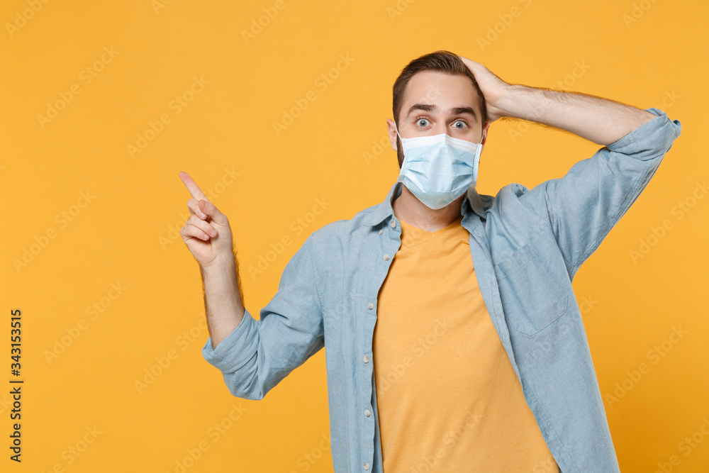 Excited young man in sterile face mask posing isolated on yellow wall background. Epidemic pandemic coronavirus 2019-ncov sars covid-19 flu virus concept. Pointing index finger up, put hand on head. Excited young man in sterile face mask posing isolated on yellow wall background. Epidemic pandemic coronavirus 2019-ncov sars covid-19 flu virus concept. Pointing index finger up, put hand on head.