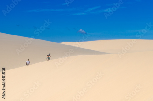 People walk along the sand dunes, view from the back, blue sky