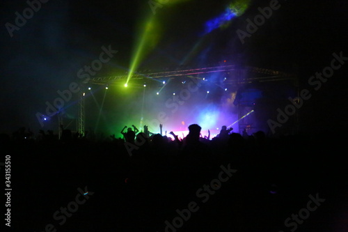 Picture of rock concert, music festival, New Year eve celebration, party in nightclub, dance floor, disco club, many people standing with raised hands up and clapping, happiness and night life concept