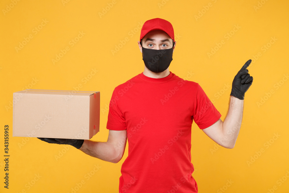 Delivery man employee in red cap blank t-shirt uniform face mask glove hold empty cardboard box isolated on yellow background studio Service quarantine pandemic coronavirus flu virus 2019-ncov concept Delivery man employee in red cap blank t-shirt uniform face mask glove hold empty cardboard box isolated on yellow background studio Service quarantine pandemic coronavirus flu virus 2019-ncov concept