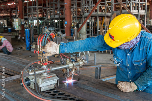 Workers are using gas cutting machines to burning bending steel plates that is curled after welding for built-up h-beam at industrial factory.
