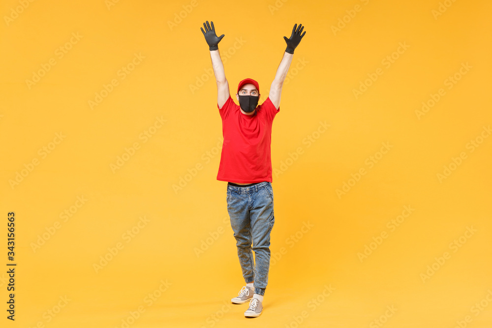 Full length delivery man in red cap t-shirt uniform sterile face mask gloves isolated on yellow background studio Guy employee courier Service quarantine pandemic coronavirus virus 2019-ncov concept. Full length delivery man in red cap t-shirt uniform sterile face mask gloves isolated on yellow background studio Guy employee courier Service quarantine pandemic coronavirus virus 2019-ncov concept.