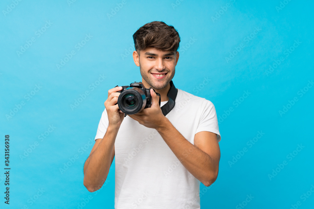 Obraz premium Young handsome man over isolated blue background with a professional camera