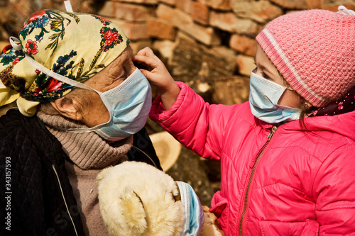 An old grandmother with her family during quarantine due to an outbreak of coronavirus infection. Grandmother with a small child in masks on their faces play games during quarantine due to coronavirus