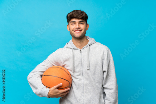Young handsome man over isolated blue background with ball of basketball