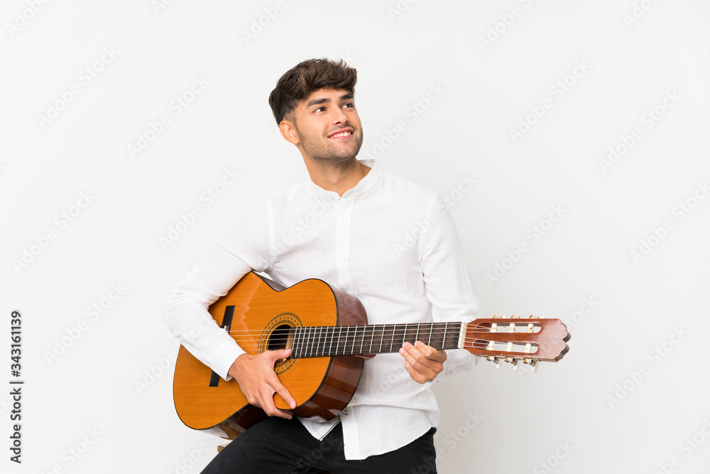 Obraz premium Young handsome man with guitar over isolated white background looking up while smiling