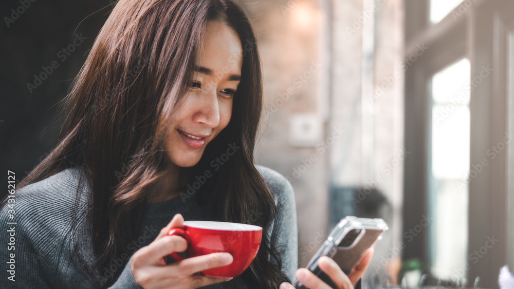 Young woman at cafe drinking coffee and using mobile phone.Asian girl with red cup of coffee and use smartphone. Young woman at cafe drinking coffee and using mobile phone.Asian girl with red cup of coffee and use smartphone.