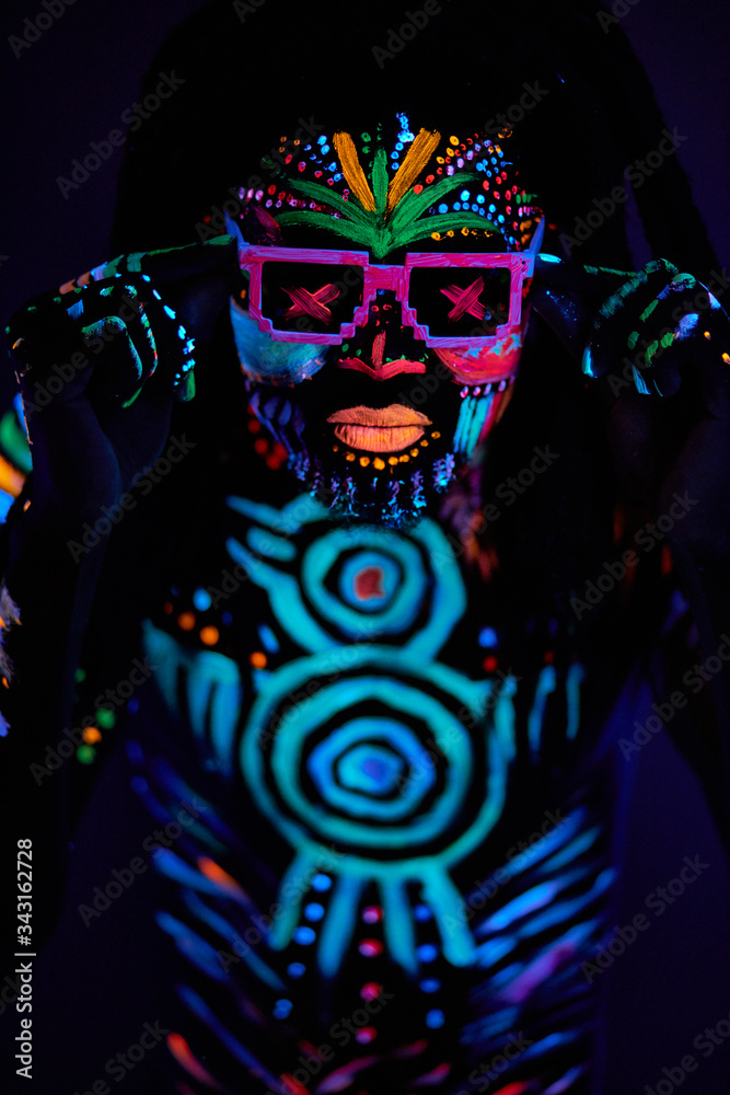 Naklejka premium portrait of fantastic disco dancer with fluorescent make-up glowing in dark isolated space. dance, dj, fluorescent luminescence concept