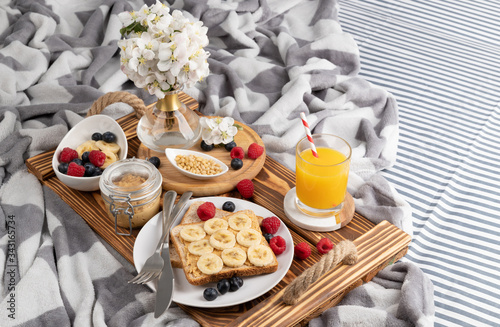 Breakfast in bed. Wooden tray with glass of orange juice and sandwich with berries