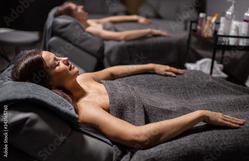 two young attractive female lie on bed in towels before face lift procedure, women came to get beauty procedures. relaxation. skincare and wellbeing concept