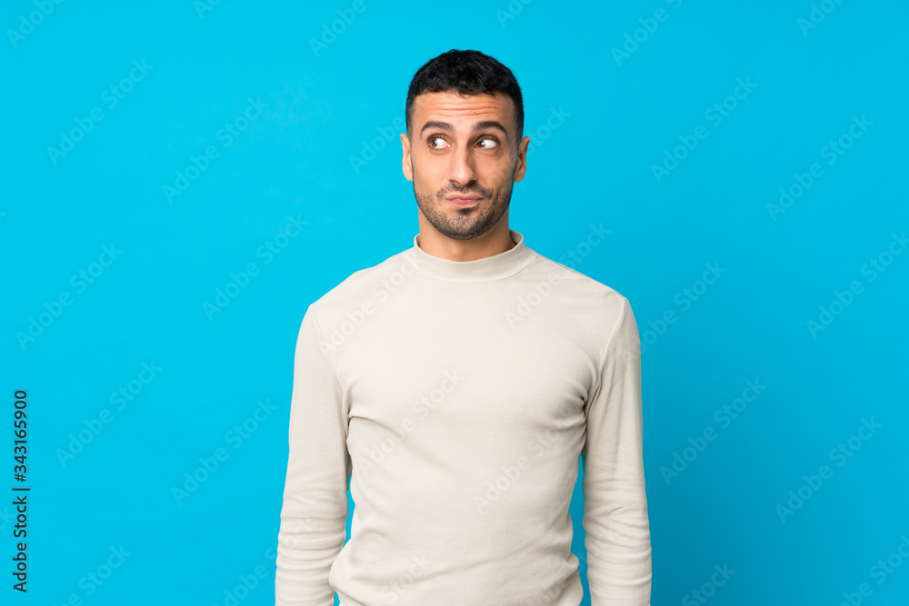 Young man over isolated blue background making doubts gesture looking side Young man over isolated blue background making doubts gesture looking side