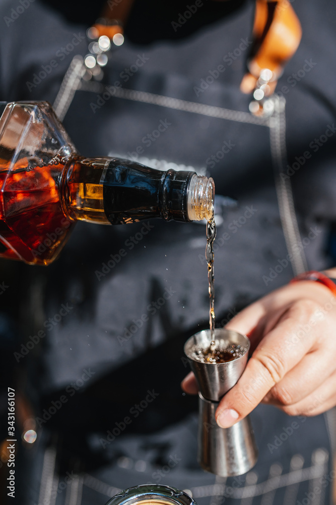 bartender is pouring drink into the steel jigger. Close-up, daylight. Bartender pours whiskey into a measuring cup