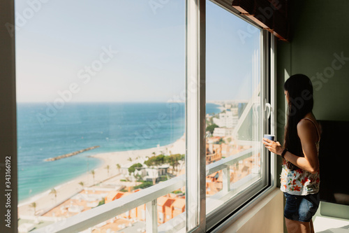 Young woman in front of the window in her apartment © Manu Reyes