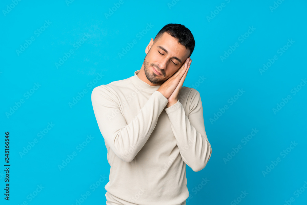 Young man over isolated blue background making sleep gesture in dorable expression Young man over isolated blue background making sleep gesture in dorable expression