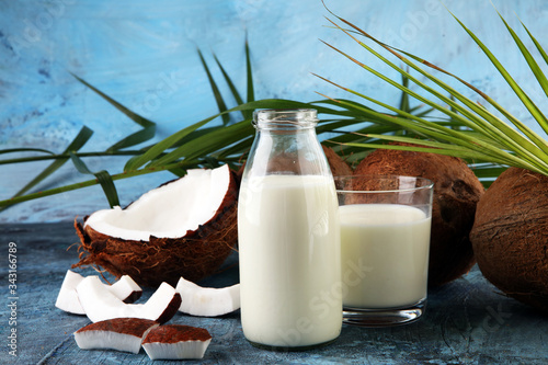 Coconut milk with fresh nut and palm leaves on rustic background.