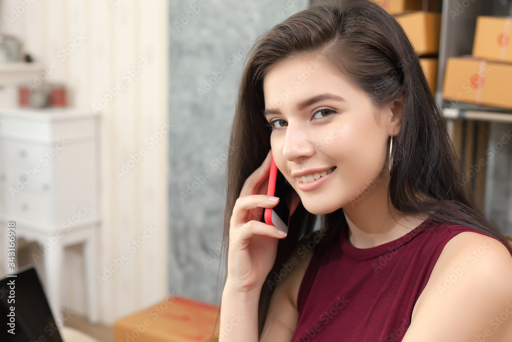 Portrait young happy smiling entrepreneur woman talking on mobile phone with customer about the online product and online delivery to home. Looking at camera. Portrait young happy smiling entrepreneur woman talking on mobile phone with customer about the online product and online delivery to home. Looking at camera.