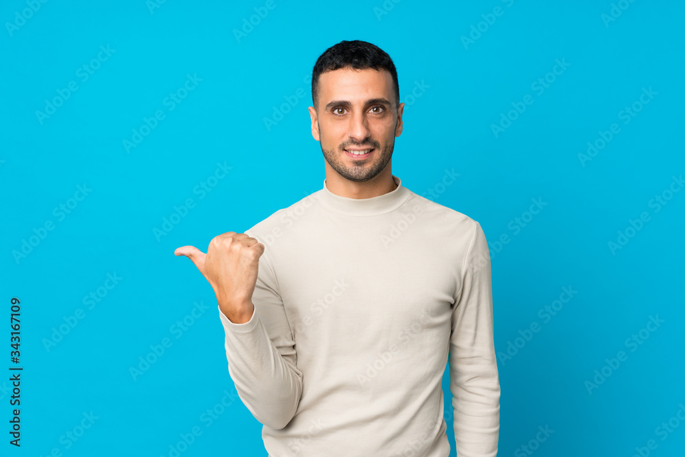 Fototapeta premium Young man over isolated blue background pointing to the side to present a product