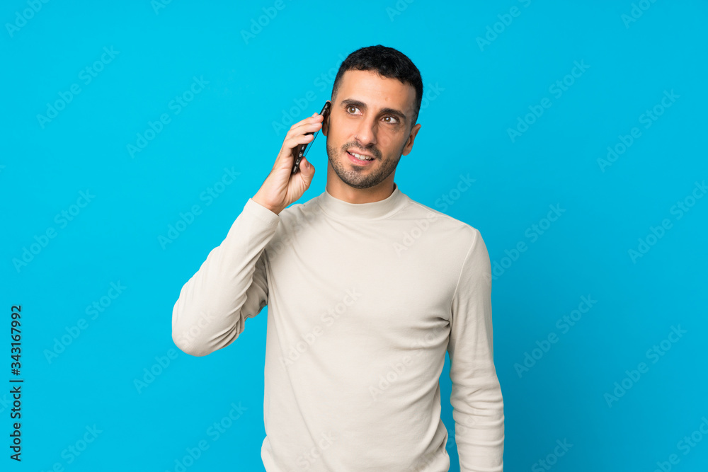 Fototapeta premium Young man over isolated blue background keeping a conversation with the mobile phone