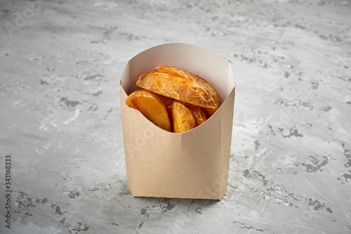 Slices of fried potatoes in street packaging on a concrete table background.