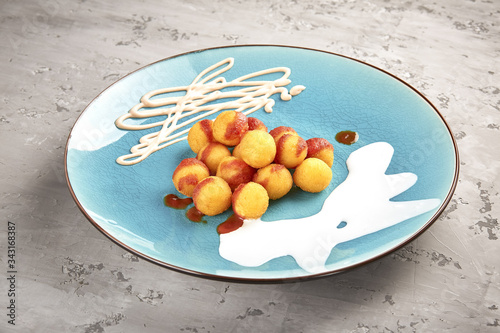 Plate with fried potato balls and sauce on a concrete table.