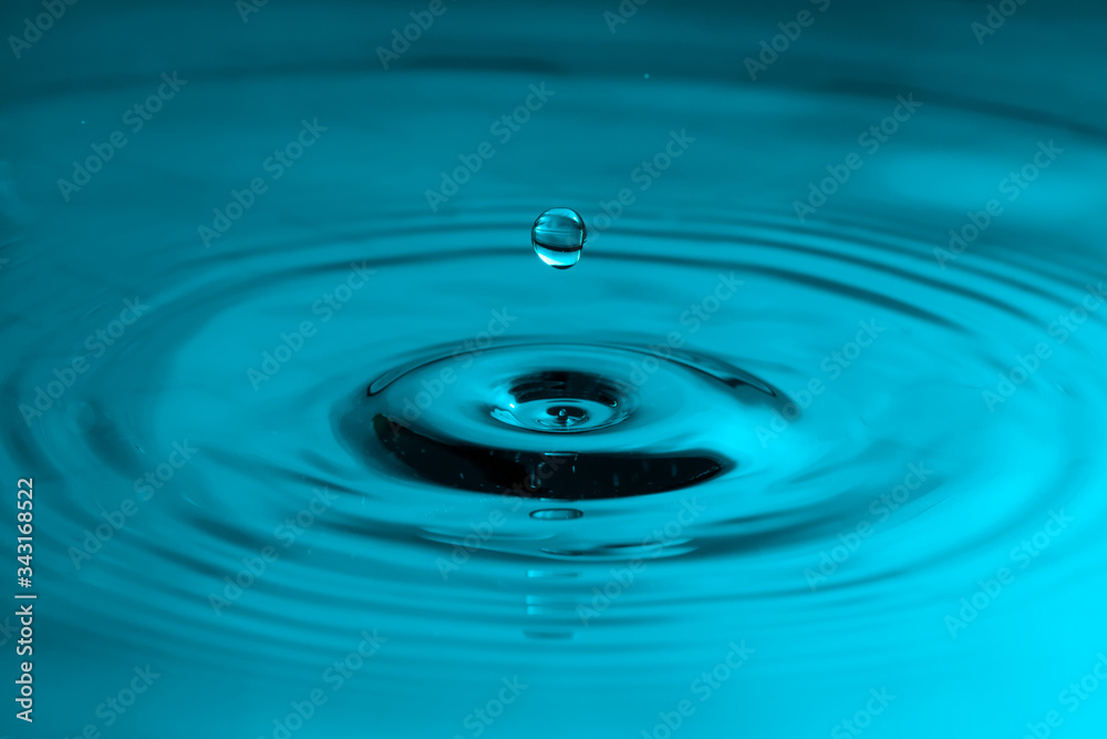 Falling drop of water with ripples in a blue color Falling drop of water with ripples in a blue color