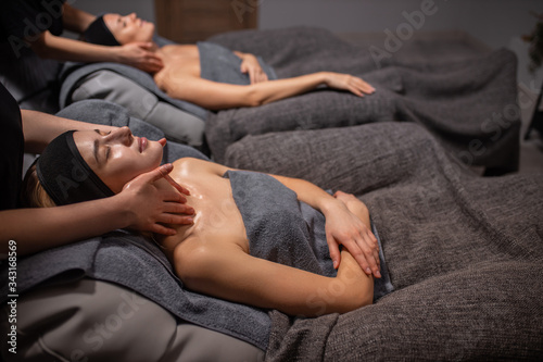 two caucasian women get face and neck massage in spa salon, natural beauty without any surgery, anti aging face lift. specialists professionally carefully do massage, skin care