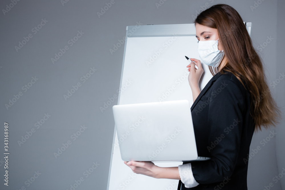 A masked business coach in quarantine communicates and teaches pupils through a web conference. White board and laptop. A masked business coach in quarantine communicates and teaches pupils through a web conference. White board and laptop.