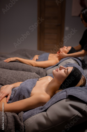 caucasian young ladies have rest during face lift massage at spa, beautiful women lie on desk for massage with closed eyes, get skin treatment