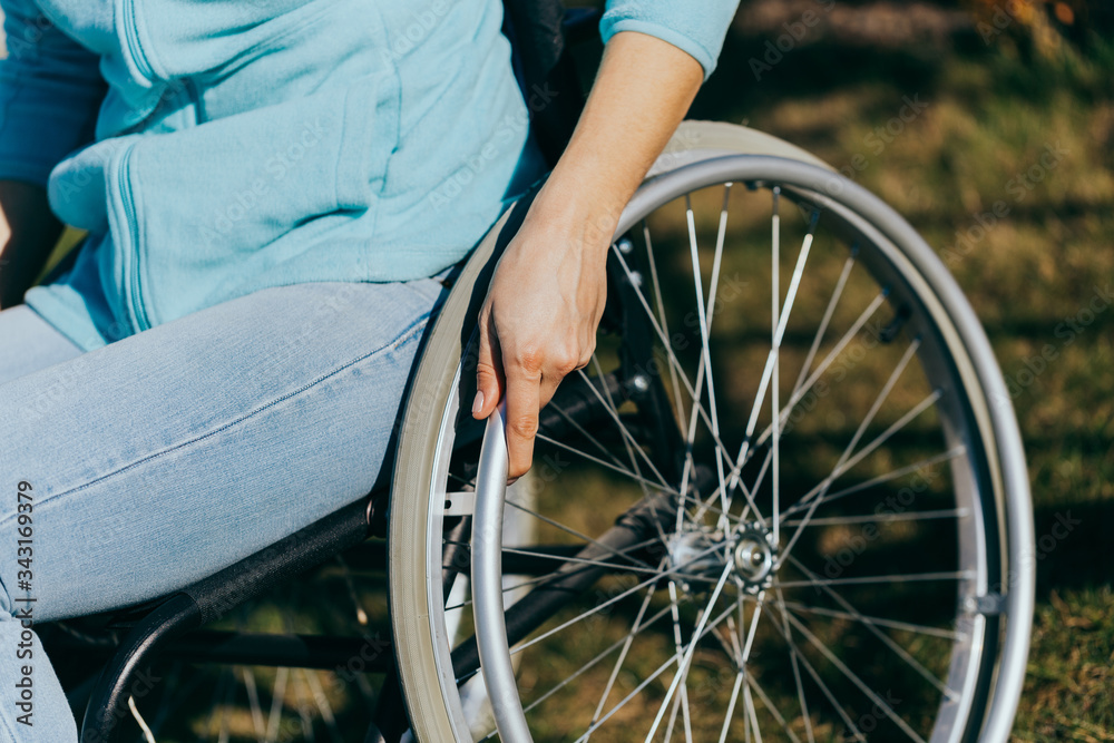 Obraz premium Close up of a young woman in a wheelchair while walking in a park on a sunny day. Recovery and healthcare concepts.