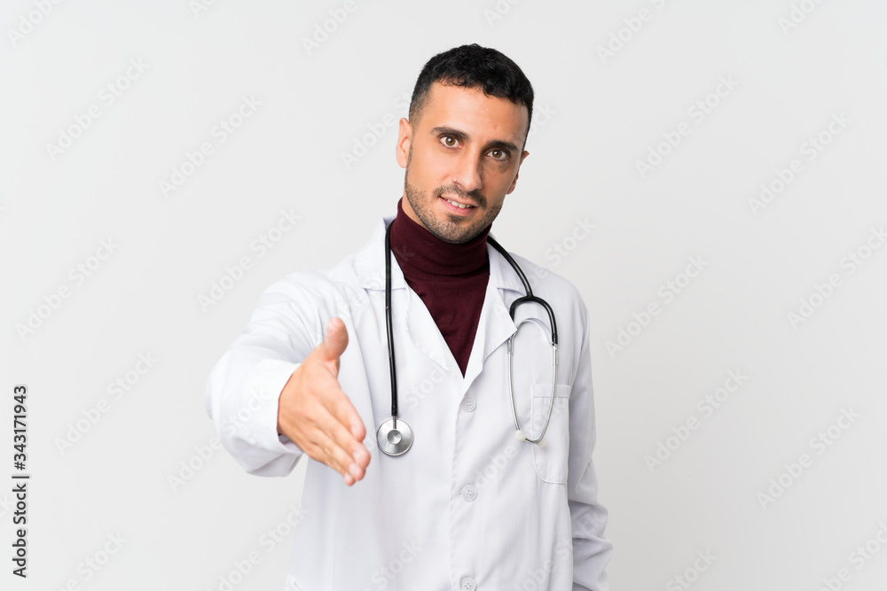 Young man over isolated white background with doctor gown and making a deal Young man over isolated white background with doctor gown and making a deal
