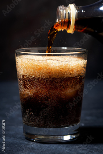 Coca Cola is pouring into a glass from a bottle, closeup