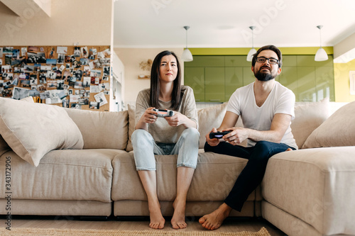 Young couple of man and woman playing video game on a console, sitting on couch in living room.
