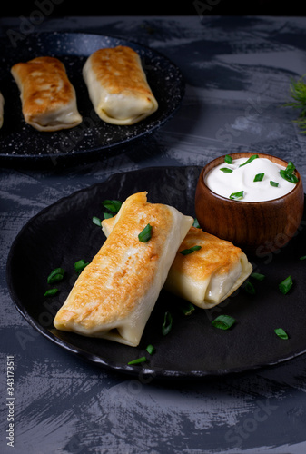 Pancakes with filling are served on the black plate with sour cream and topped with green onion