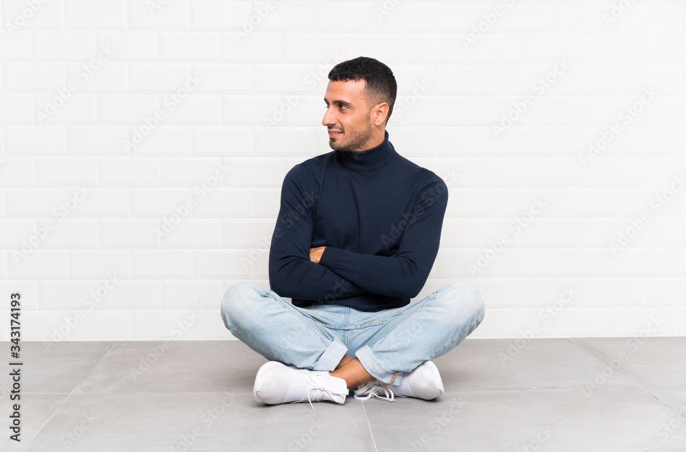 Young handsome man sitting on the floor looking to the side