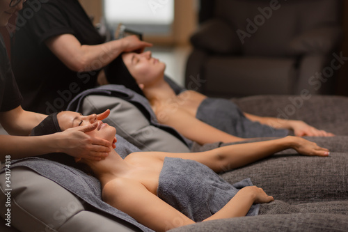 two attractive women are pampered themselves at the health spa, get face lift massage in wellbeing salon. professional beauticians make anti aging massage on neck and face