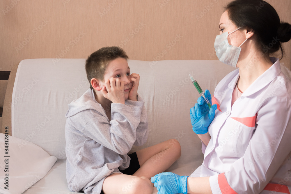 a doctor in a white coat and blue medical gloves holds a syringe with medicine in front of a boy, a child in gray pajamas is afraid of the injection, calling a doctor at home. Protection AGAINST covid a doctor in a white coat and blue medical gloves holds a syringe with medicine in front of a boy, a child in gray pajamas is afraid of the injection, calling a doctor at home. Protection AGAINST covid