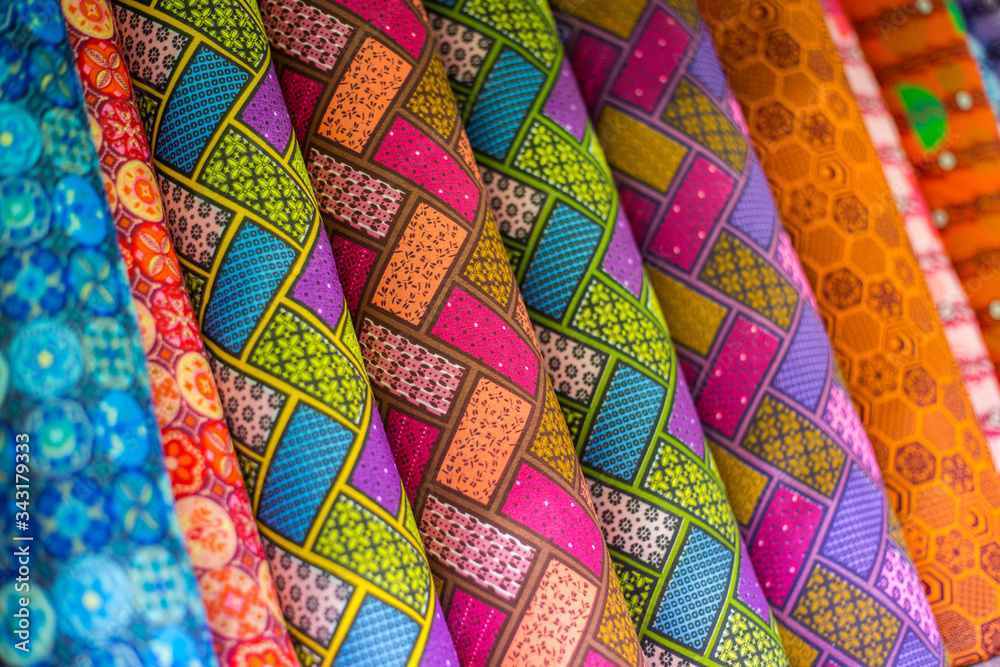 Rolls of fabric with African inspired patterns on display for customers in a sewing shop, to be used for clothing.
