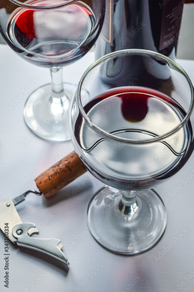 Closeup of glasses of red wine and bottle with shadows and reflections on a white textured surface. Closeup of glasses of red wine and bottle with shadows and reflections on a white textured surface.