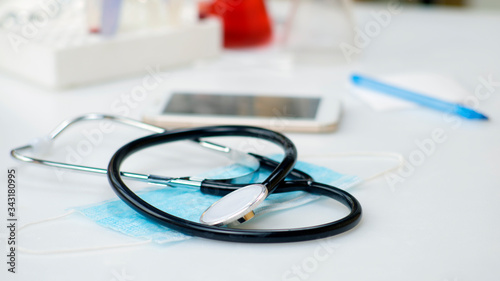 A stethoscope lies on a medical mask next to a smartphone, on the doctor s desktop. Online medical consultation and medical clinic, communication and communication with the patient, online doctor.