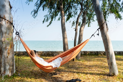 Summer vacations concept, Happy asian woman with white dress, sleeping rest and relaxing in hammock on tropical beach at sunshine day.