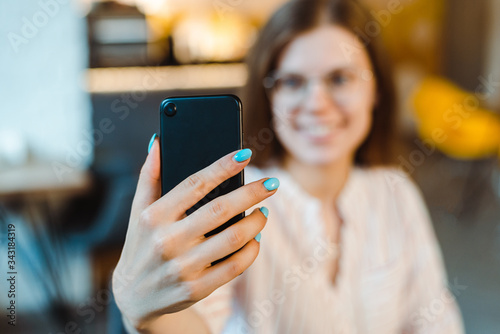 selective focus of girl in glasses taking selfie on smartphone in cafe