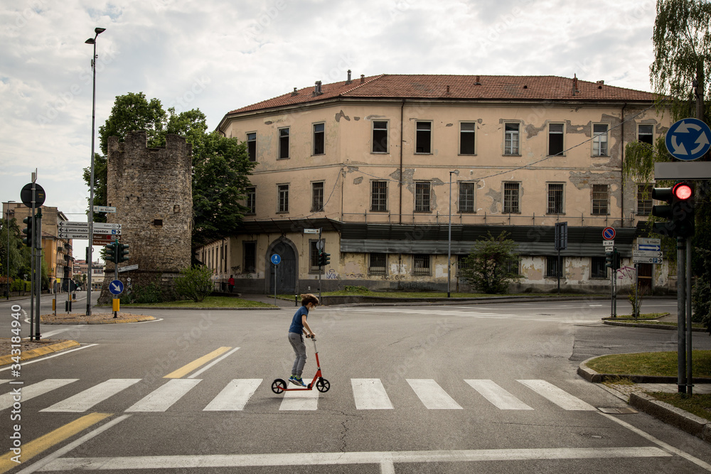 Obraz premium Bambino attraversa città deserta col monopattino, Bergamo