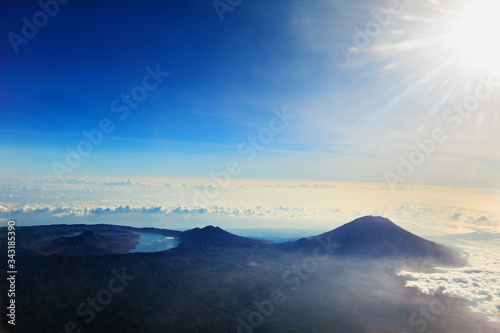 View from airplane window. Aerial photo of Agung - highest peak of island Bali, mount Abang, active volcano Batur with volcanic lake in caldera. Popular travel destination on summer family holidays