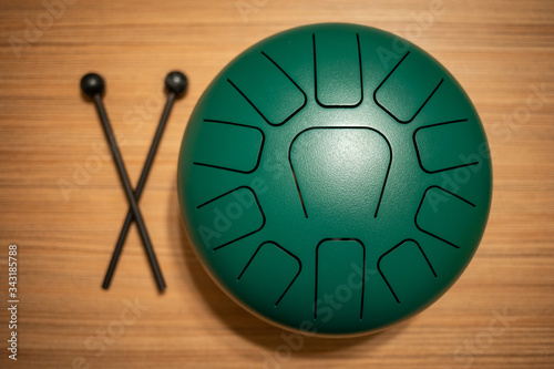 Green hand pan steel tongue drum musical instrument with 11 notes and a pair of drum hammers on a wooden background. Relaxing activities at home. photo