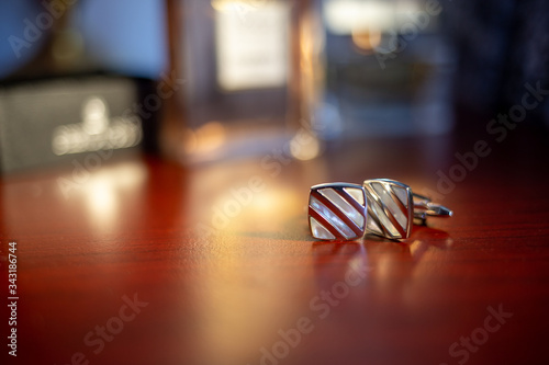 Luxury buttons on a wooden table that reflects the perfume bottles. Detail with a pair of cufflinks on the wedding day. Copy space.