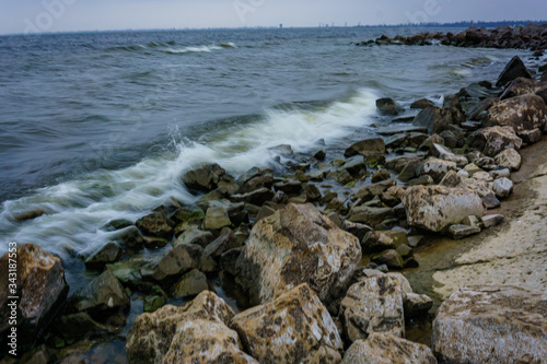 Landscape with waves crashing against the coastal stones at sunrise.