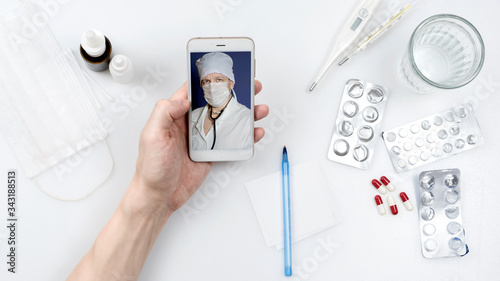 medicine, technology and healthcare concept - close up of patient hand with pills and water on table, having video chat with doctor on smartphone